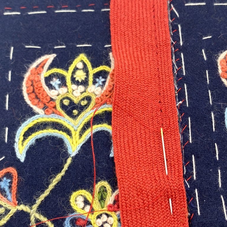 Start by binding the slit. Place the binding on the right side of the wool fabric and keep your eyes on the edge of the slit at all times. Stitch the binding with a small backstitch. Note that it can be tricky to stitch the binding at the bottom of the slit. Try to fold the pocket in such a way that you may continue to stitch in a straight line. Once you‘ve stitch the binding, it should stand upright in the bottom on the slit.